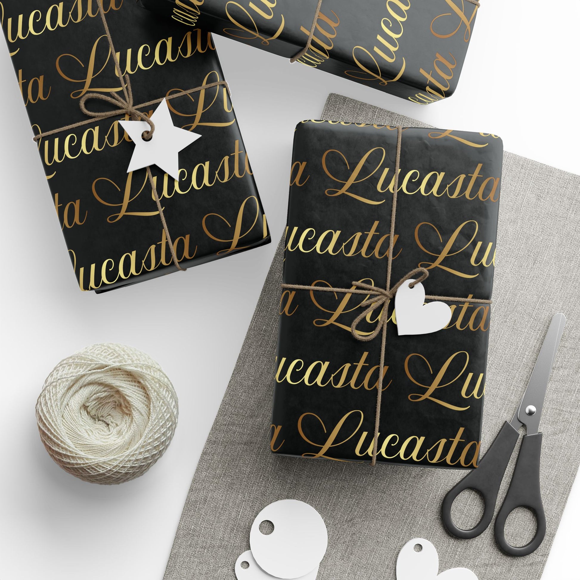 Lucasta black wrapping paper styled with gift-wrapped packages, decorative tags, and scissors on a white surface
