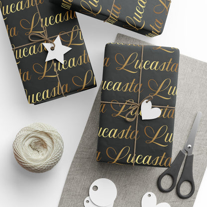 Lucasta black gift wrap with gold text, decorative tags, scissors, and yarn styled on a white surface