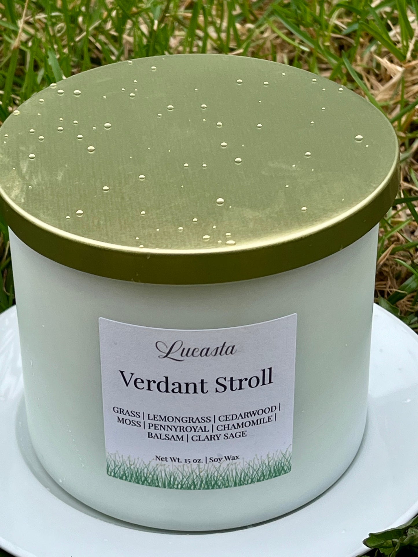 Candle jar labeled 'Verdant Stroll' with a gold lid on grass
