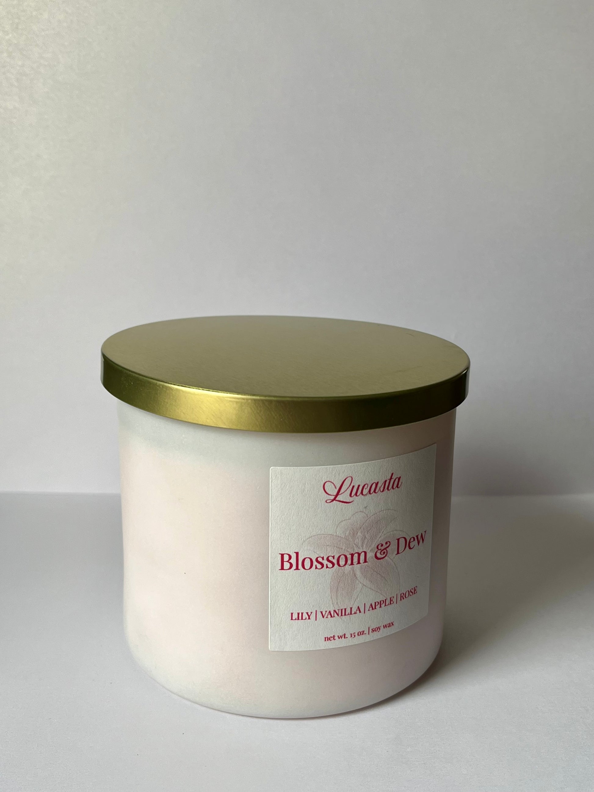 White candle with gold lid and 'Lucasta' label on a white background
