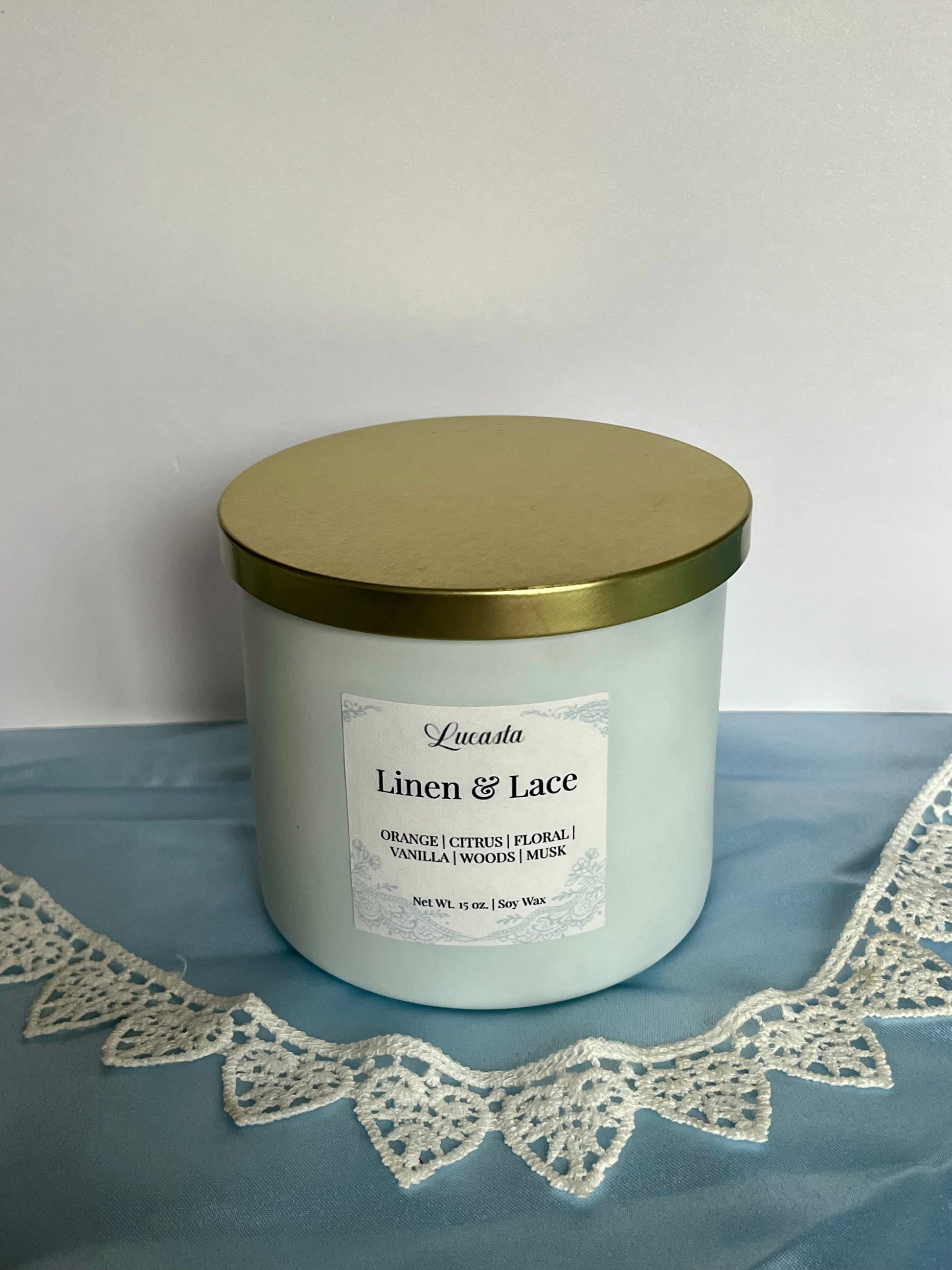 Candle with a gold lid and label on a blue surface with lace trim
