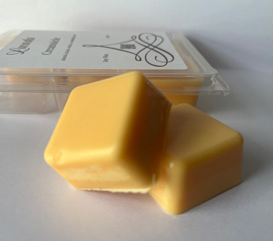 Two Lucasta Creamsicle orange wax melts in front of a clear container with branding on a white background