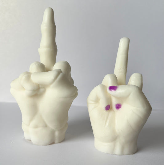 Two wax melt hand sculptures, both making middle finger gesture, one is skeletal, one has purple fingernails on a white background