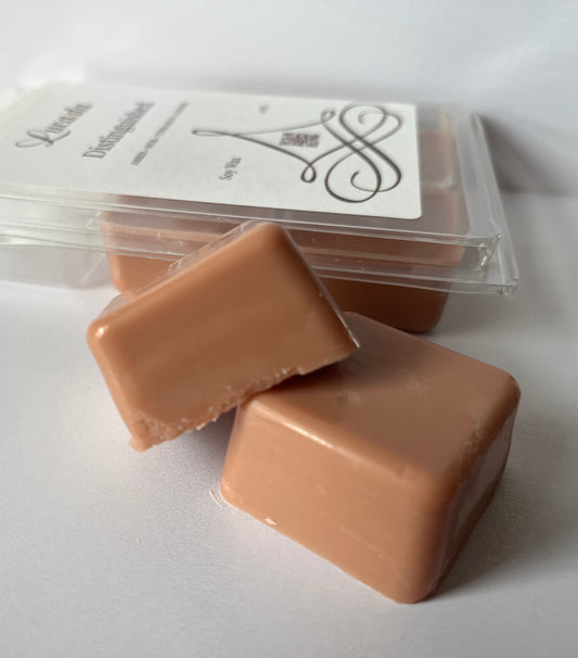 Two Lucasta Distinguished wax melts in front of a clear container with a label on a white background