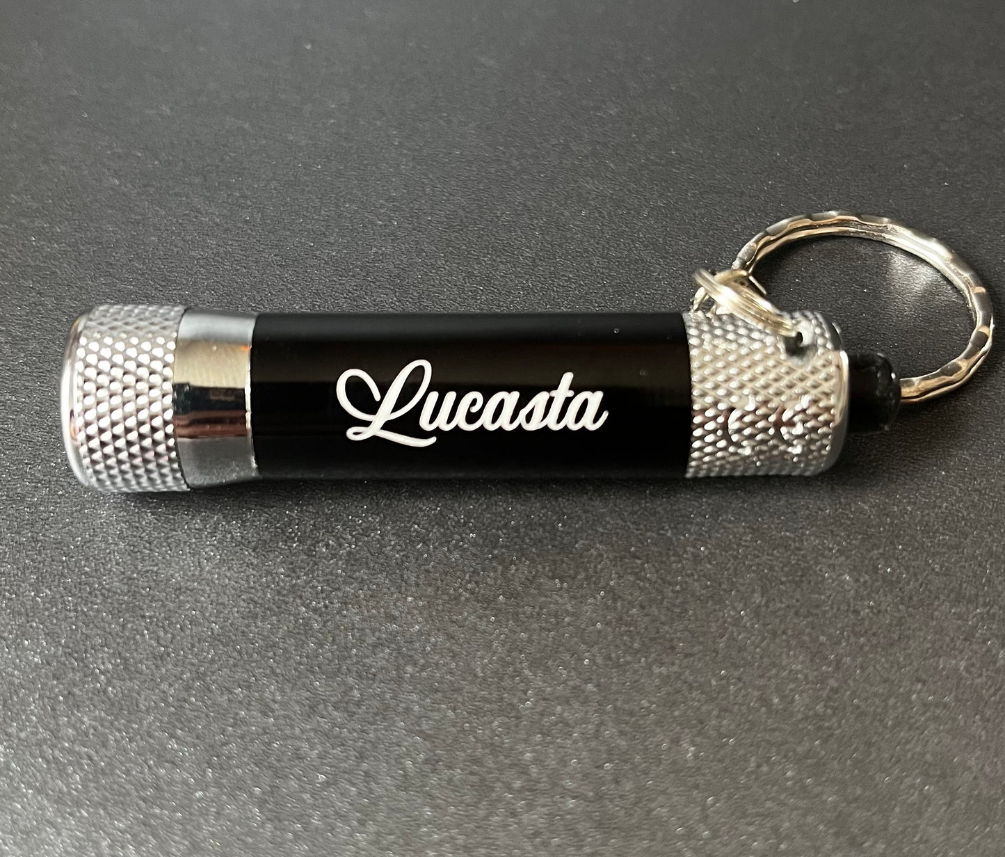 Lucasta Mini Flashlight Keychain in black and silver with Lucasta branding, product view on gray background