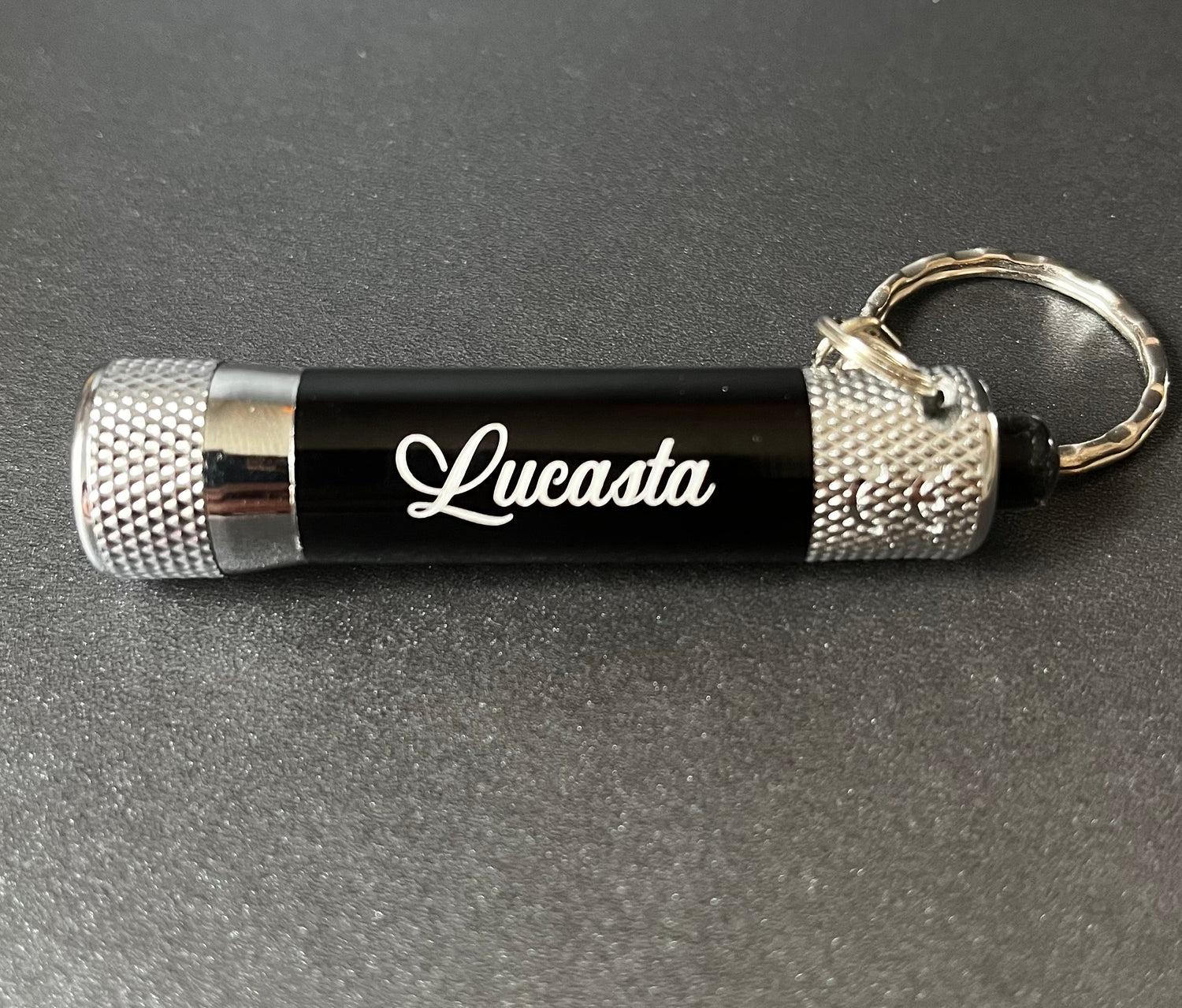 Black and silver keychain with 'Lucasta' branding on a gray background