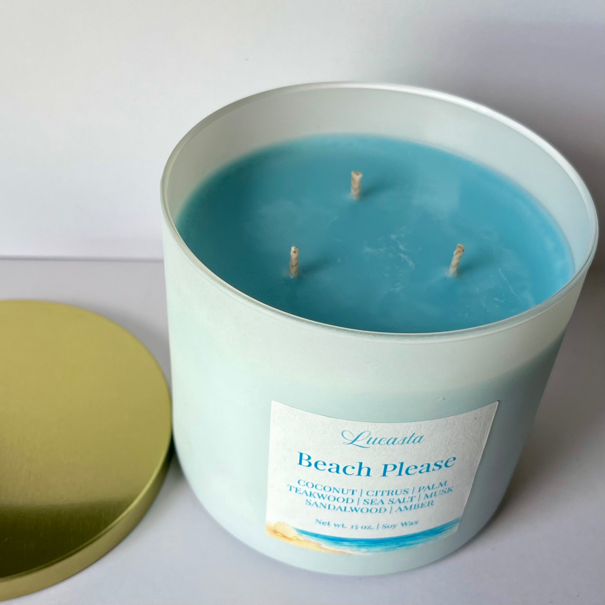 Lucasta Candles Beach Please soy candle with lid removed showing ocean blue soy wax and three wicks, gold lid beside white jar