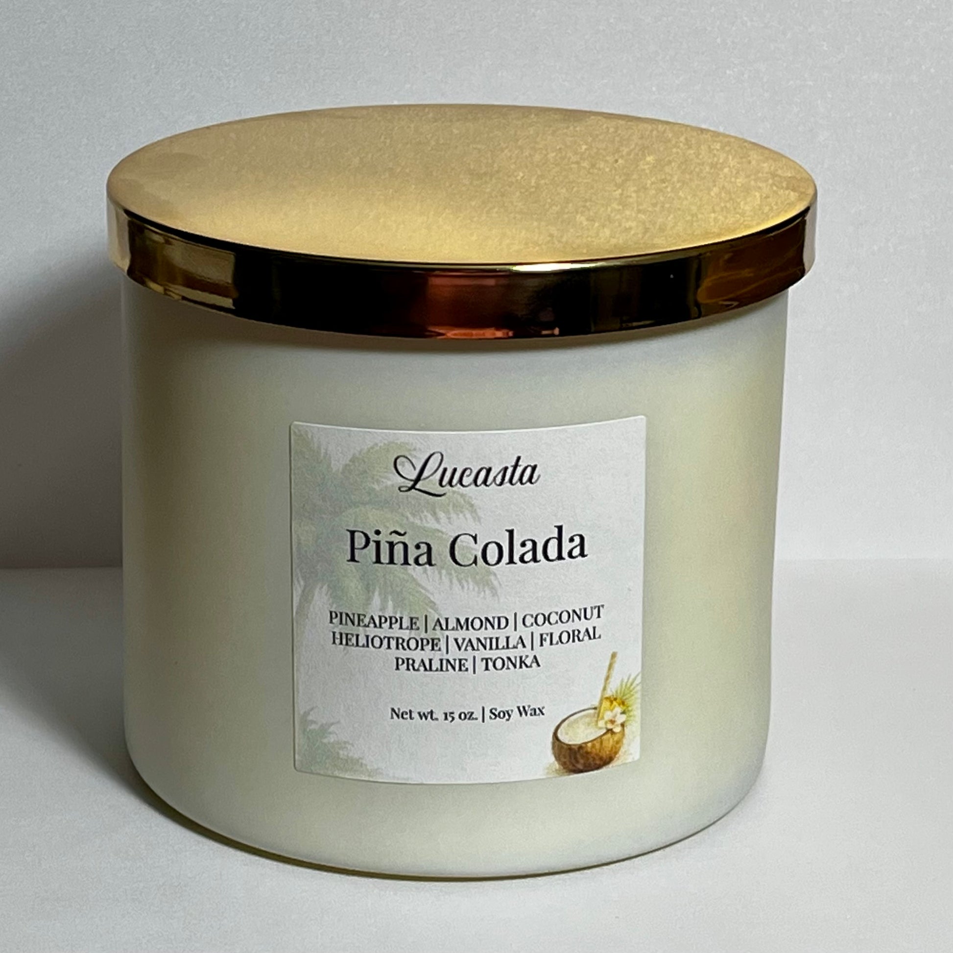 Close-up of Lucasta Piña Colada candle jar with gold lid and scent notes label reading pineapple, almond, coconut, heliotrope, vanilla, floral, praline, tonka