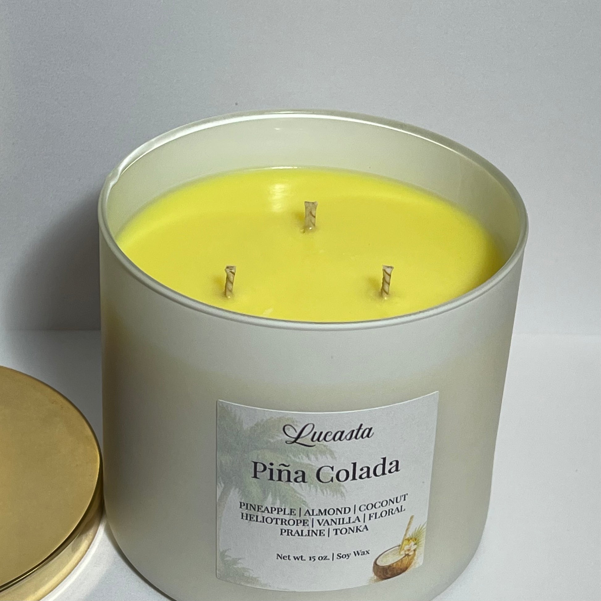 Lucasta Piña Colada triple-wick soy candle with gold lid resting beside it, showing the bright yellow wax and three wicks