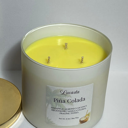 Lucasta Piña Colada triple-wick soy candle with gold lid resting beside it, showing the bright yellow wax and three wicks