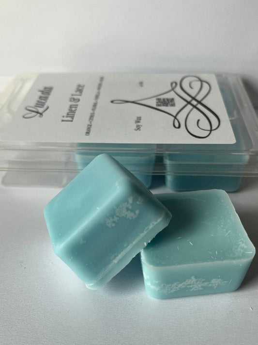 Two light blue wax melts with a brand label in the background on a white surface.